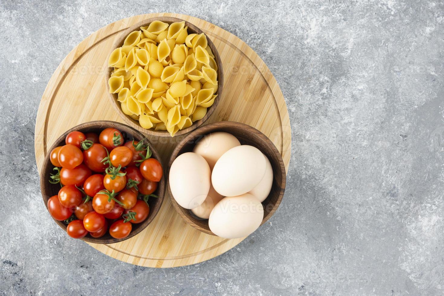 Raw chicken eggs with uncooked shell-shaped pasta and red cherry tomatoes photo