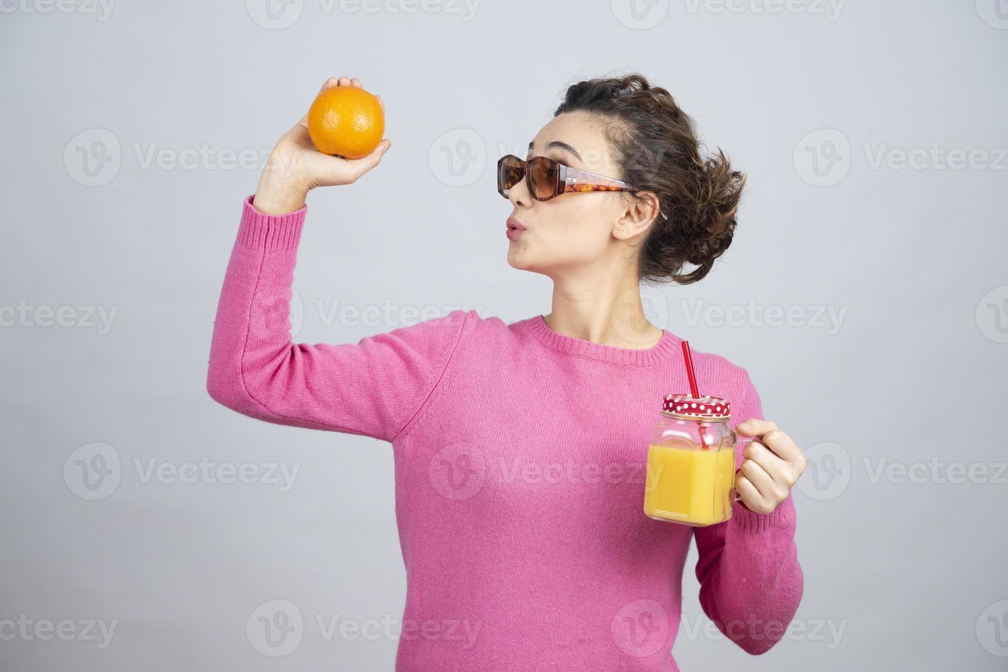 mujer joven en un suéter rosa mostrando una naranja fresca y jugo foto