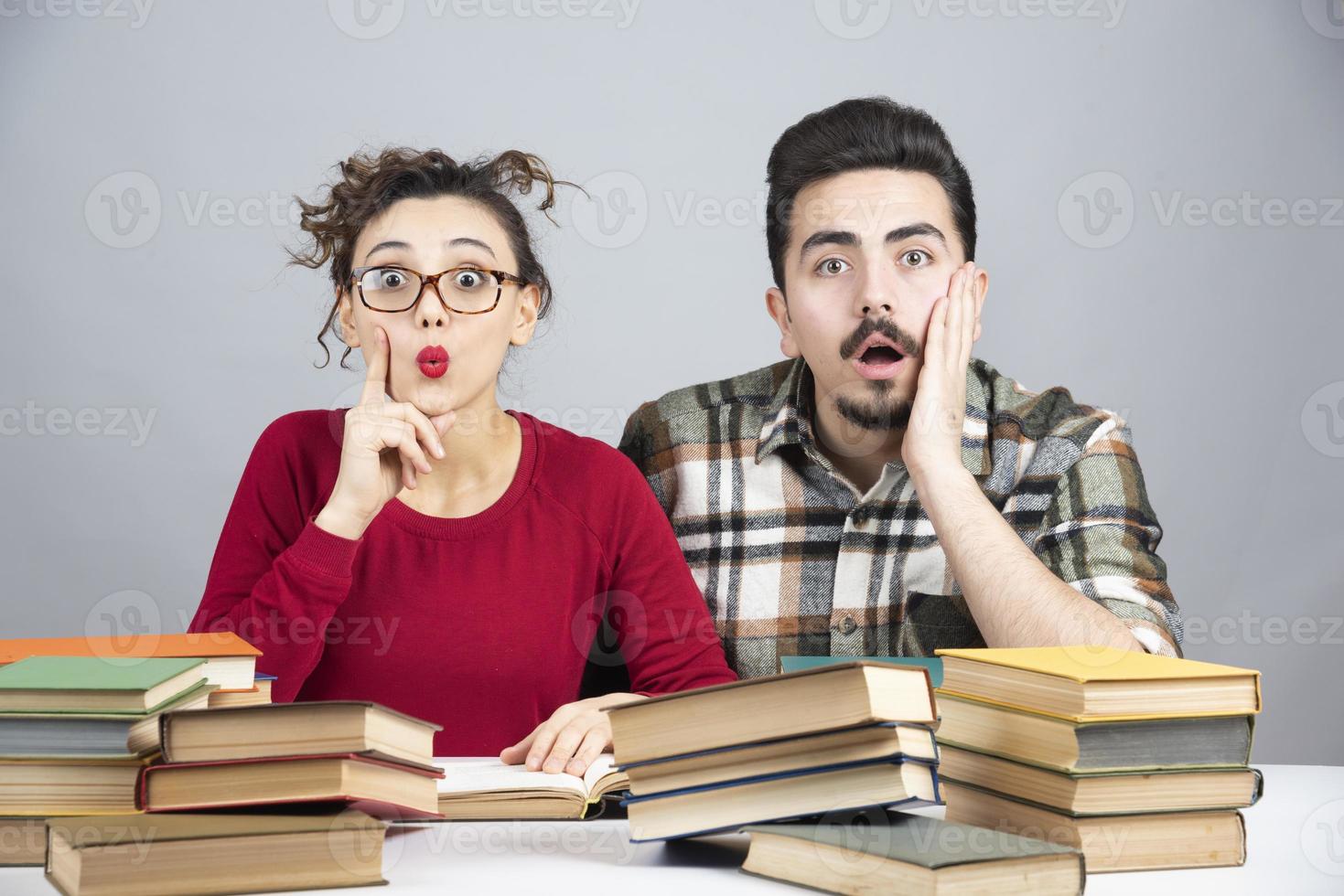 Young male and female students sitting with a lot of books and preparing for class session photo