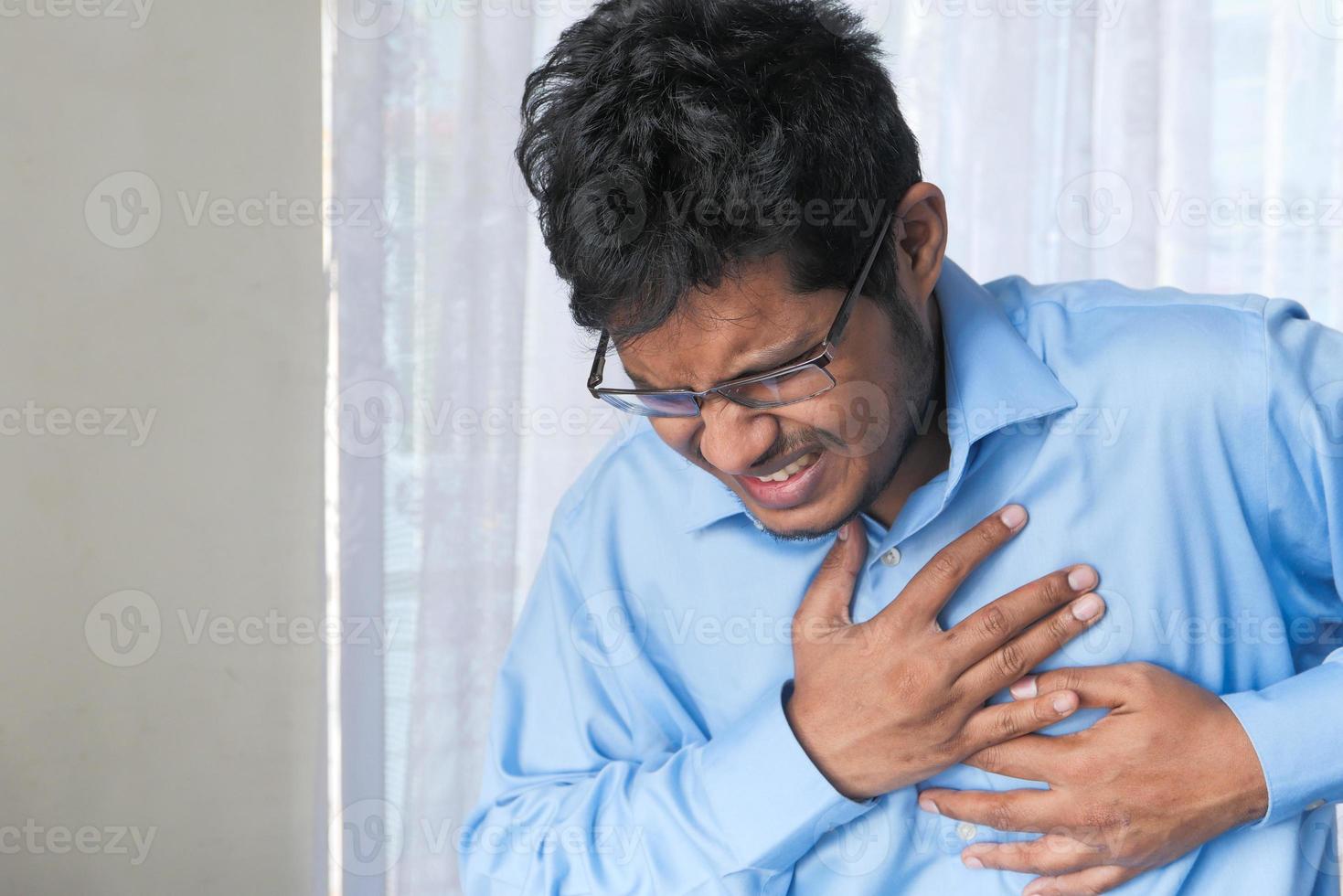 hombre en camisa azul sosteniendo el pecho en el dolor foto