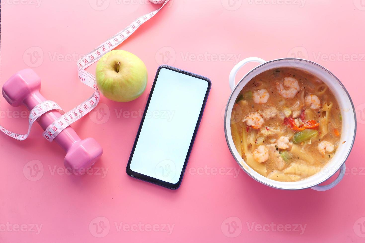 Fitness concept with tape measure, apple, smart phone, and dumb bell on pink background photo