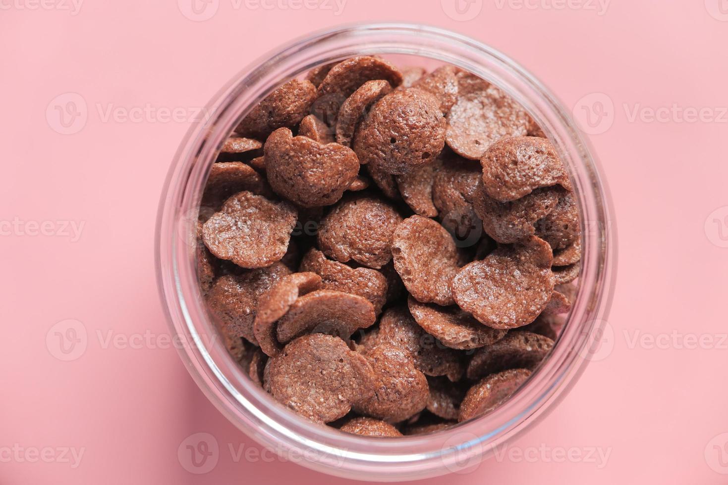 Vista superior de copos de maíz de chocolate en un recipiente sobre fondo de color rosa foto