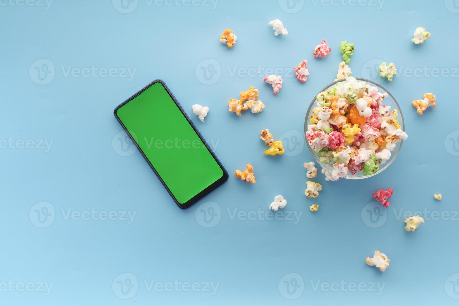 Top view of smart phone and popcorn on blue background photo