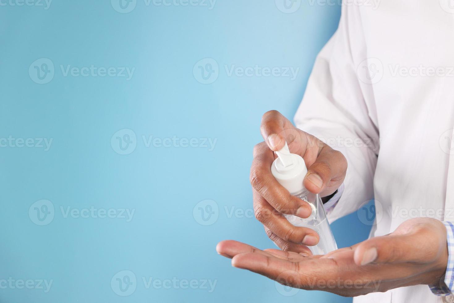 Doctor using hand sanitizer on blue background photo