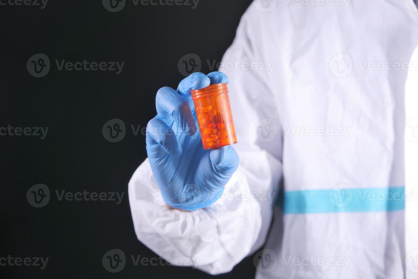 Doctor in PPE holding pills on black background photo