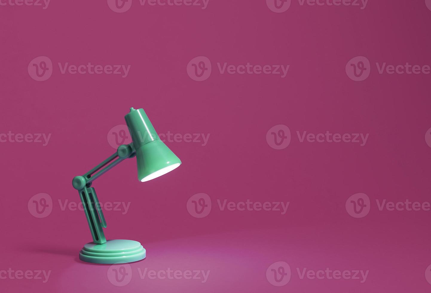 Retro green desk lamp turned on and bent over shining on a bright pink background photo