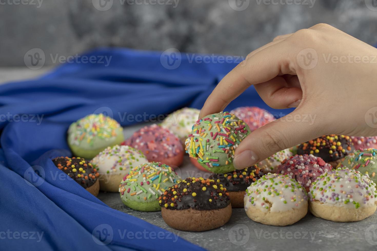 Mano de mujer tomando un pequeño donut dulce colorido con chispas foto