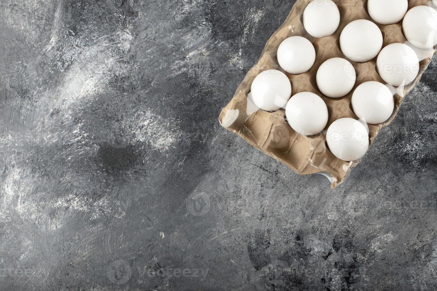 Raw chicken eggs in an egg box on a marble background photo