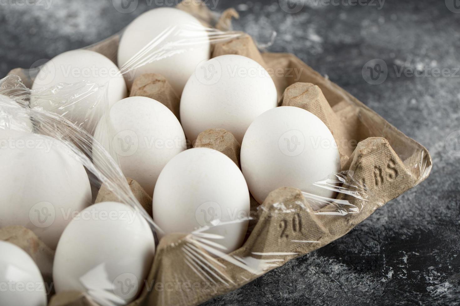 Raw chicken eggs in an egg box on a marble background photo