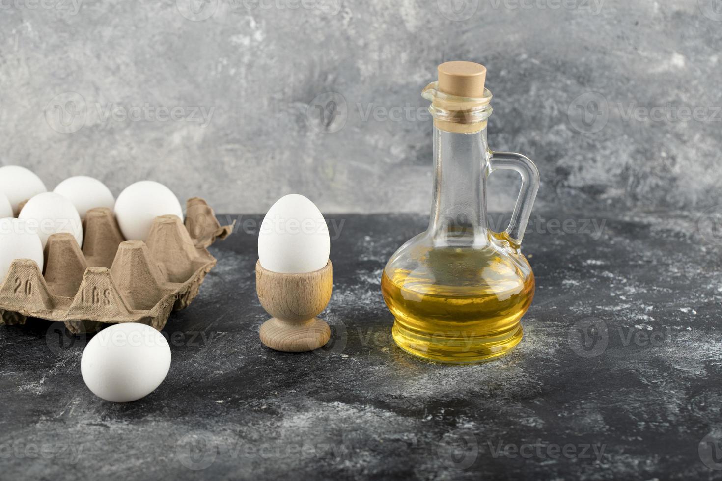 Huevo de gallina crudo en una huevera con una huevera y un vaso de aceite sobre un fondo de mármol foto