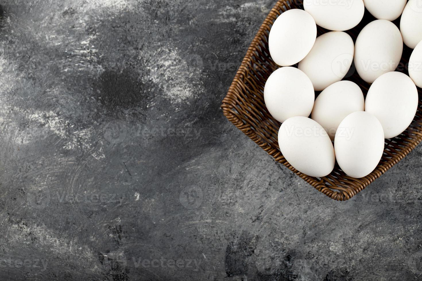 Un mimbre de madera lleno de huevos de gallina crudos blancos. foto