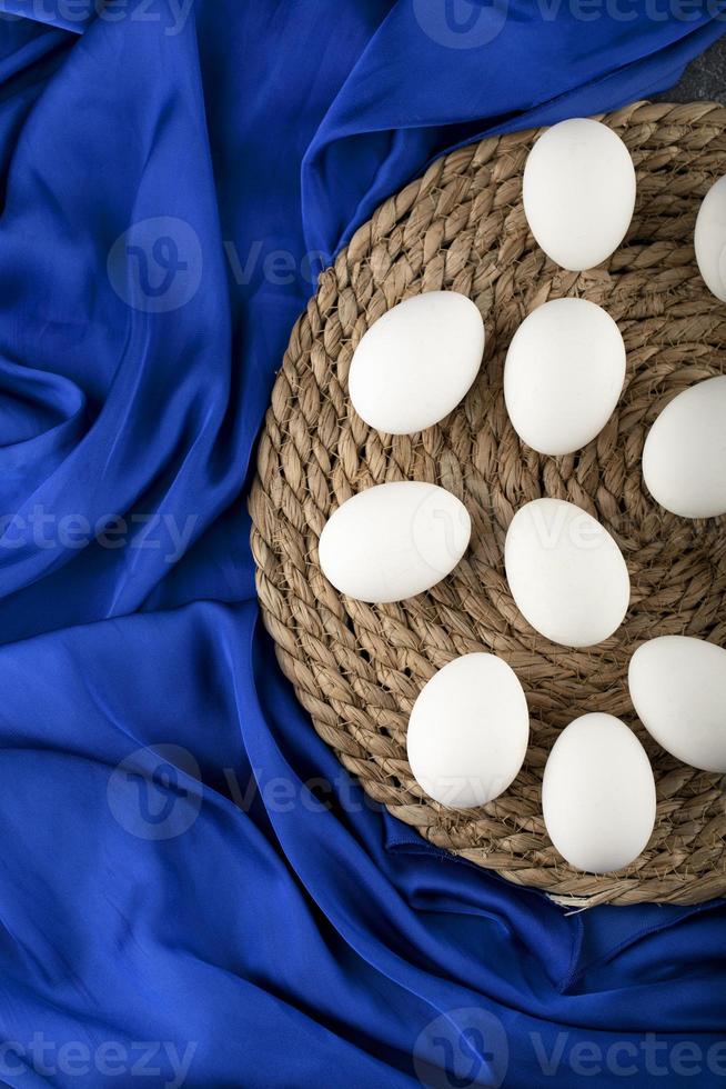 White raw chicken eggs on a wooden piece on blue cloth photo