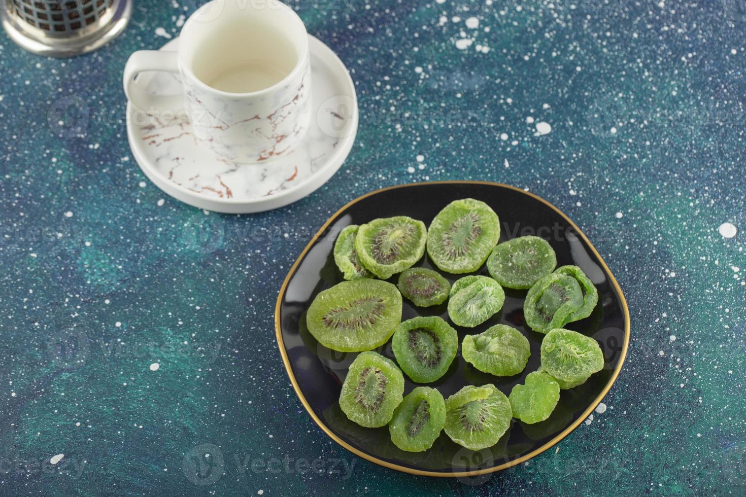 A black plate full of dried kiwi fruit and a cup of tea photo