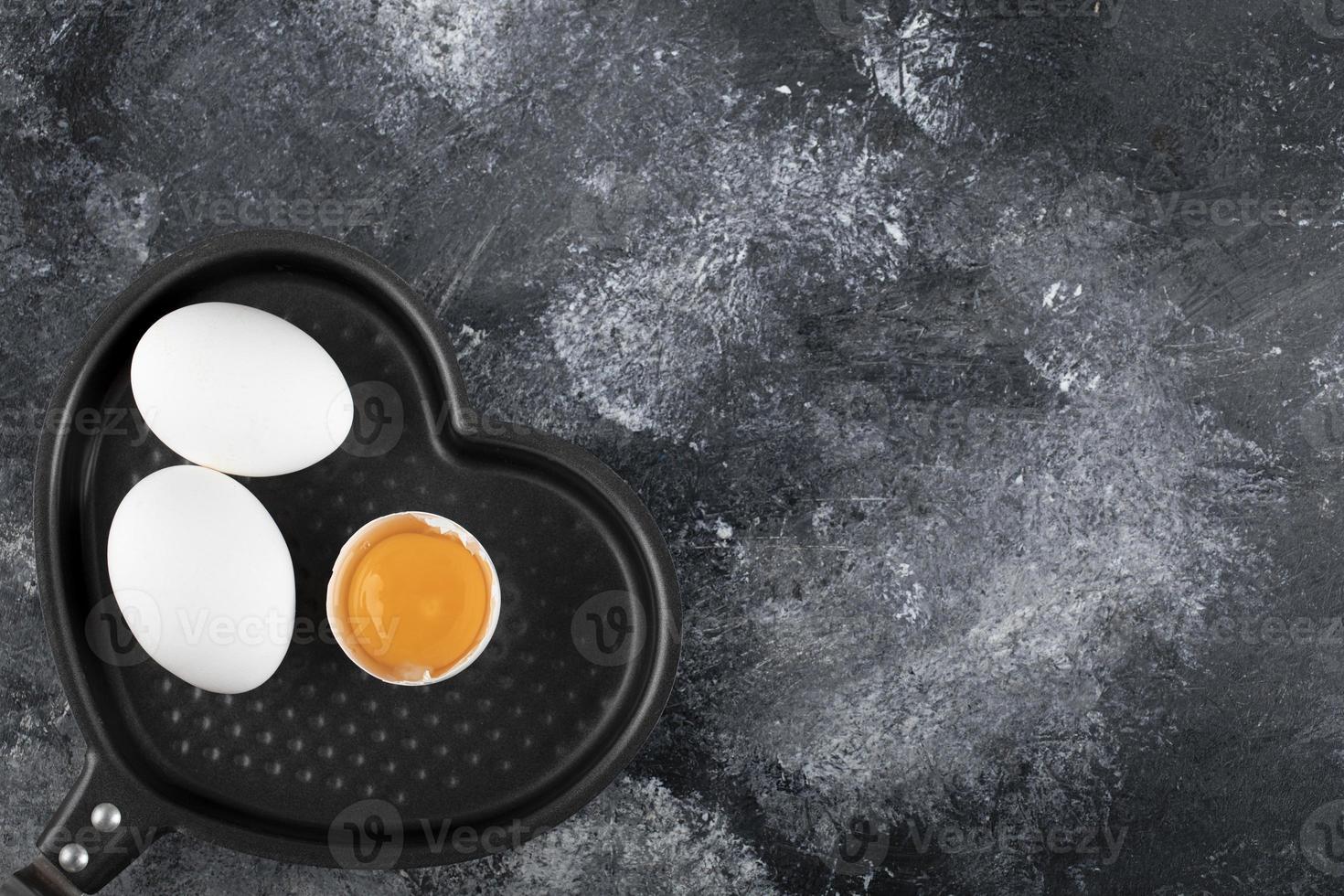 Two white eggs and yolk on a heart-shaped pan photo