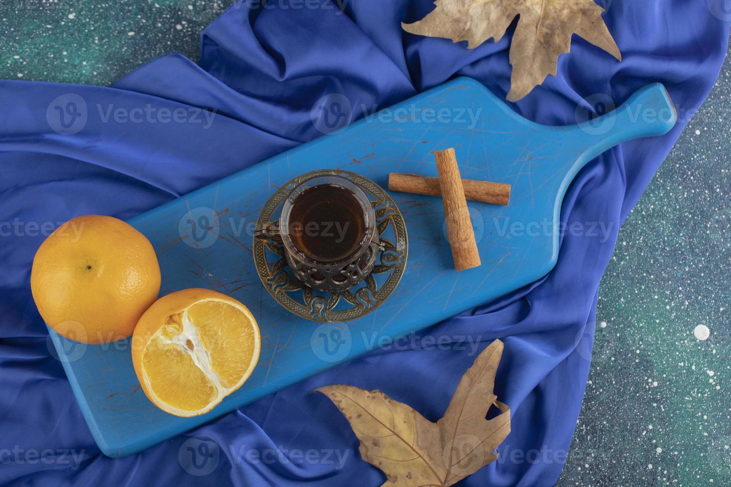 Vaso de té, naranja y ramitas de canela en un tablero azul foto