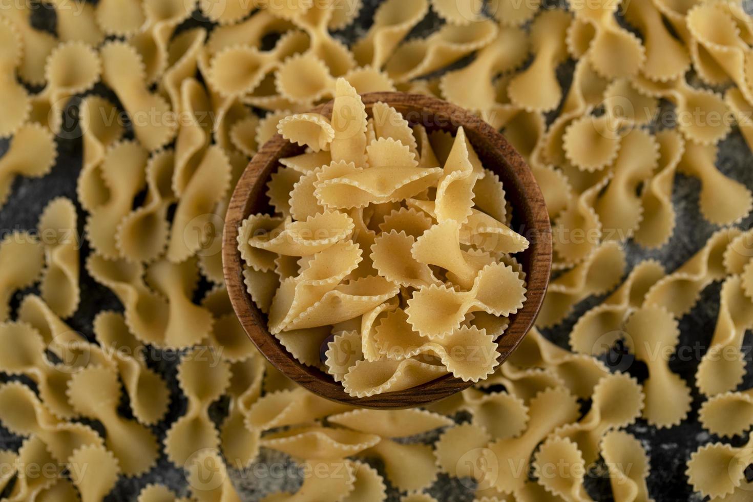 Pile of raw macaroni scattered around a wooden bowl photo