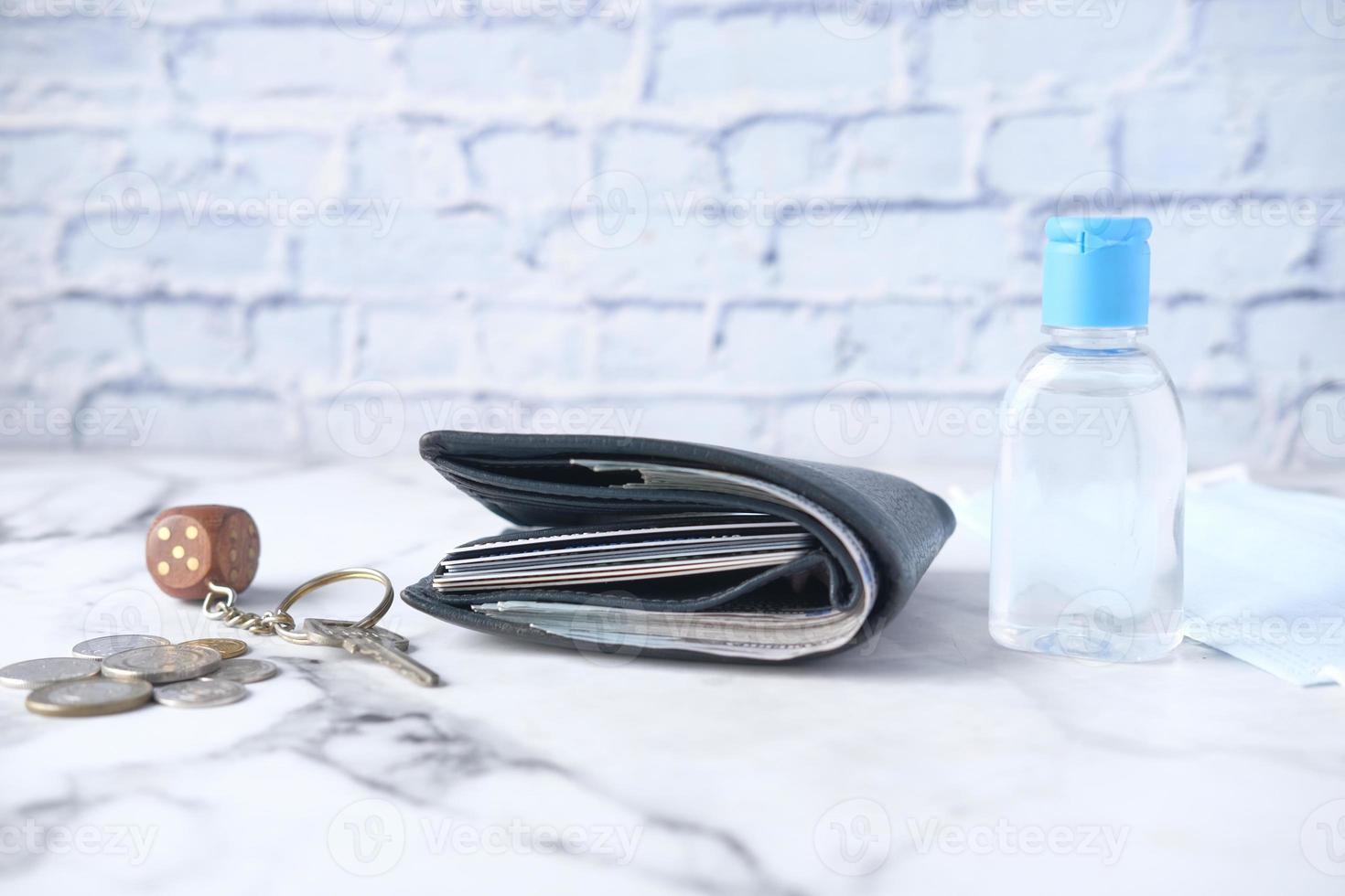 A wallet, hand sanitizer, keys, and coins on table photo