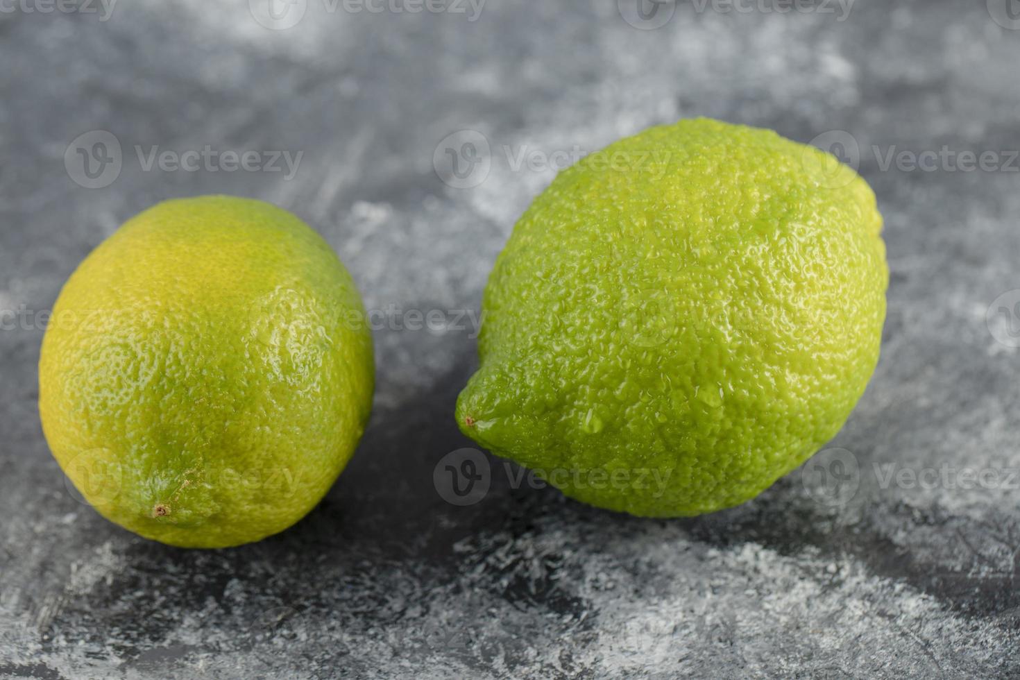 Two green fresh lemons on a marble background photo