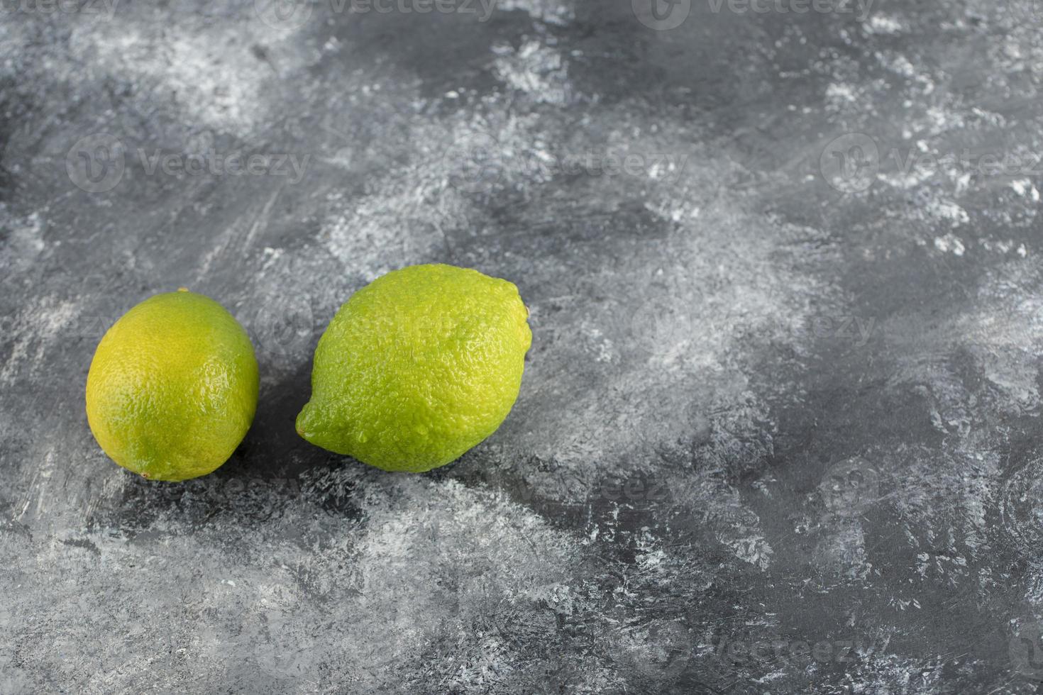 Two green fresh lemons on a marble background photo