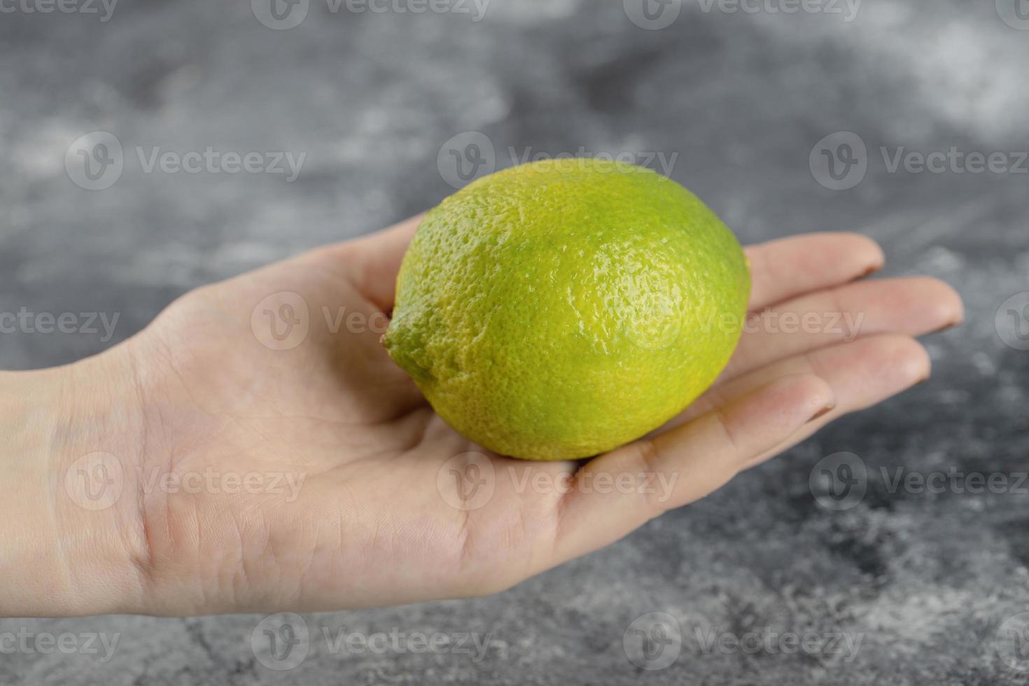 mano de mujer sosteniendo un limón verde fresco foto