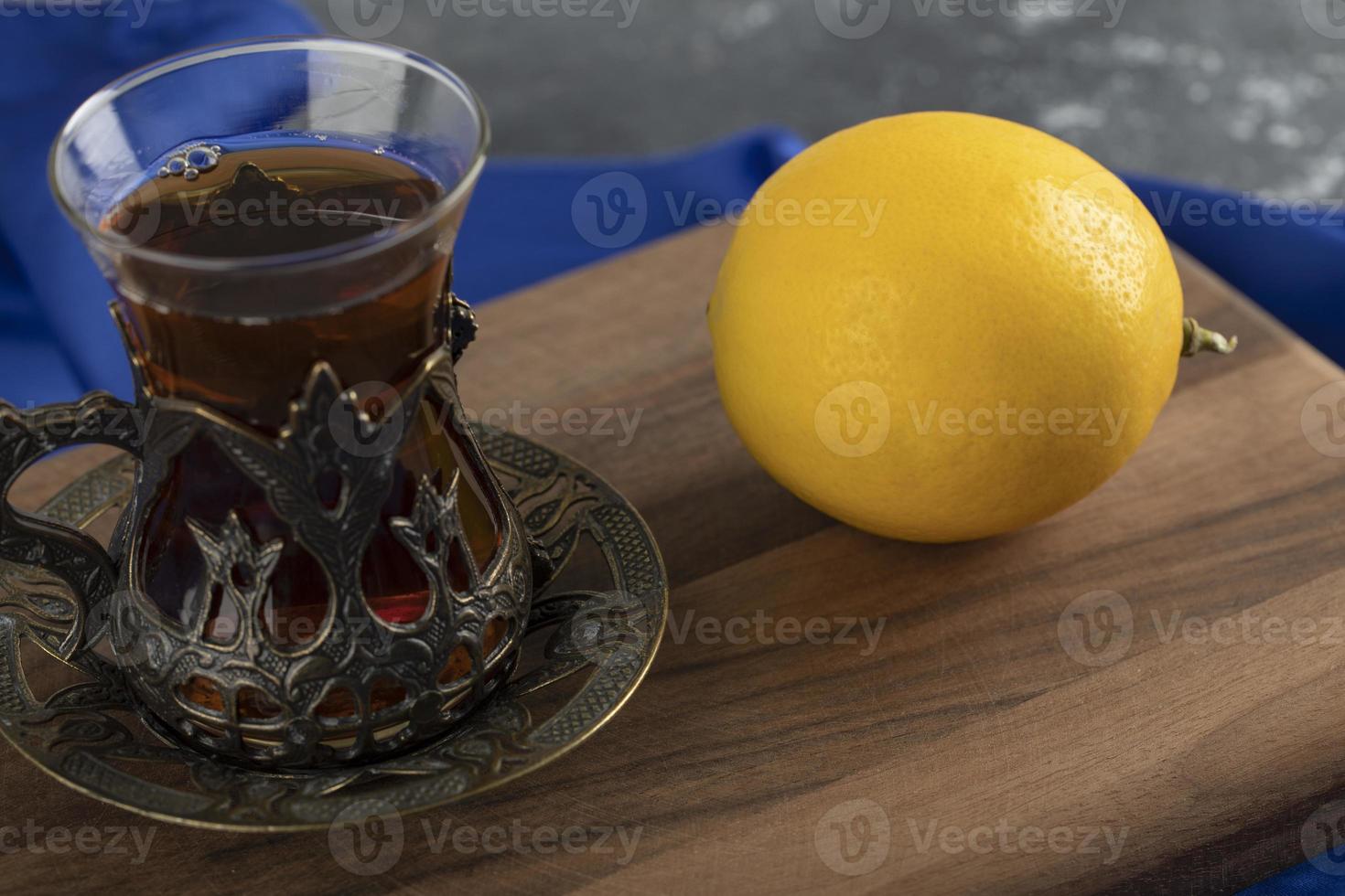 un té de cristal con un limón sobre una tabla de cortar de madera foto