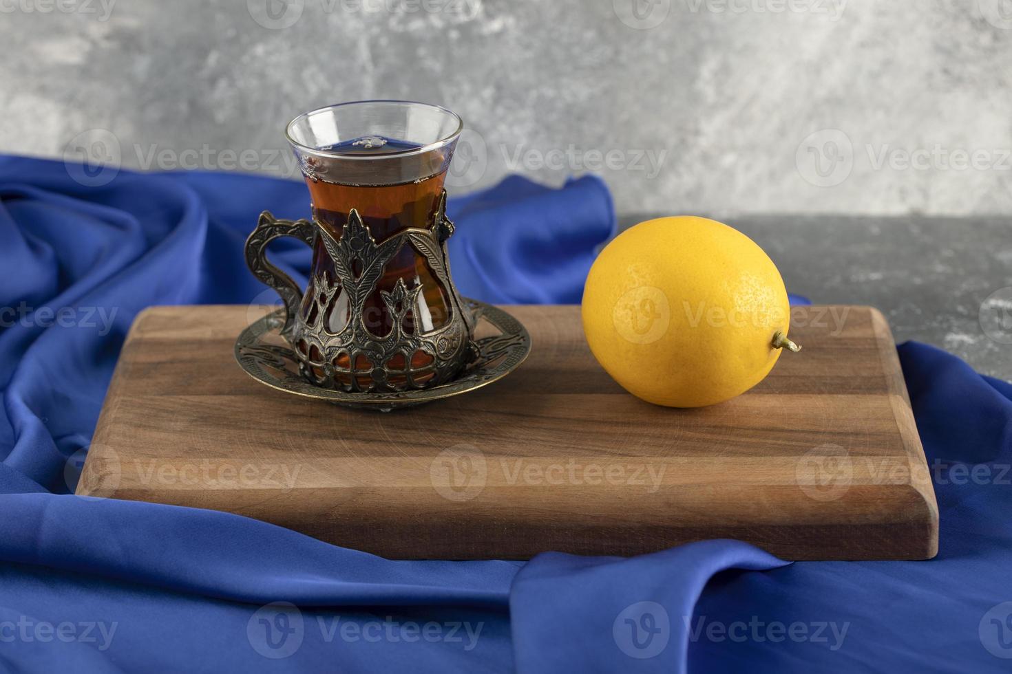 A glass tea with a lemon on a wooden cutting board photo