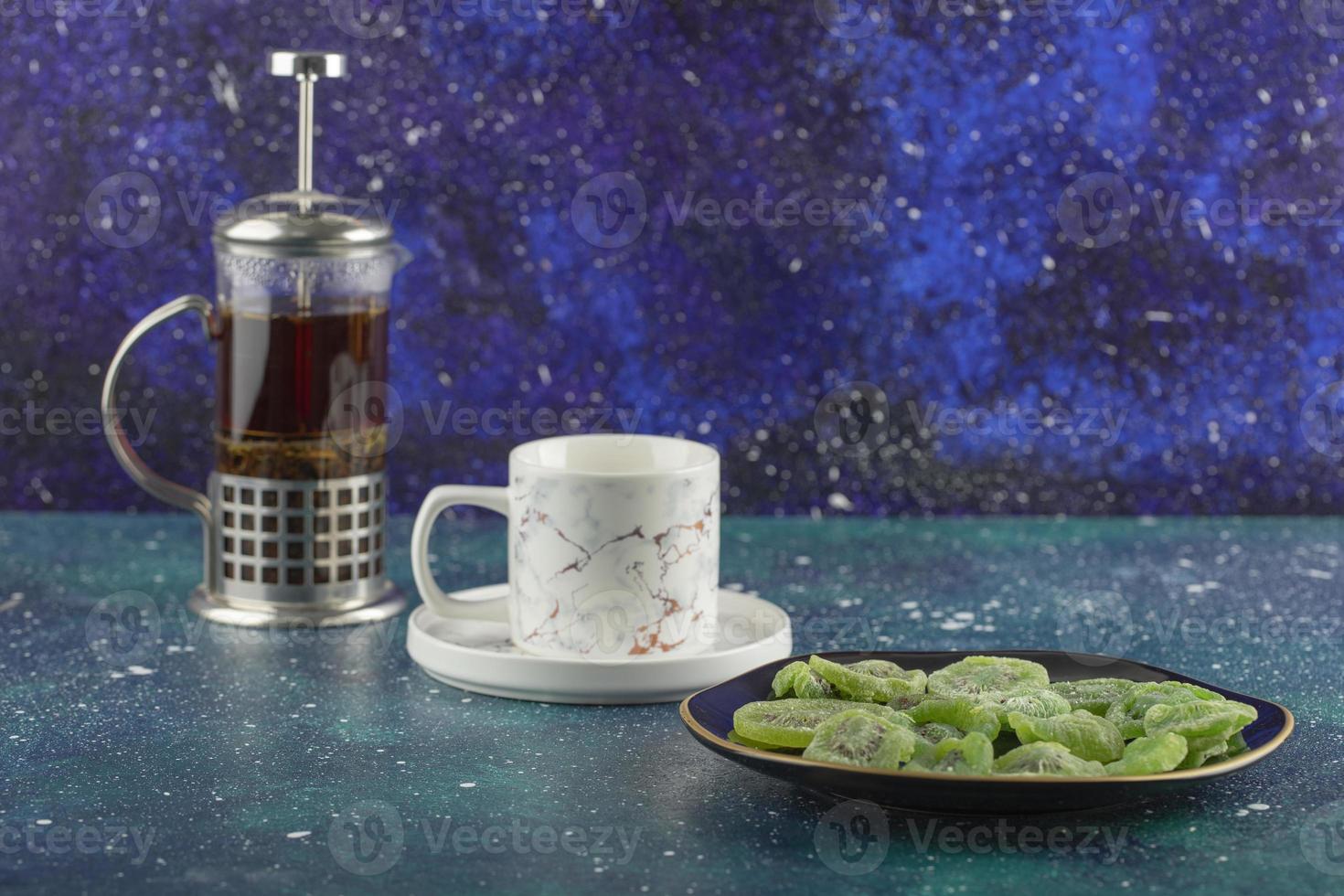 A glass teapot with dried kiwi fruit on a bright background photo