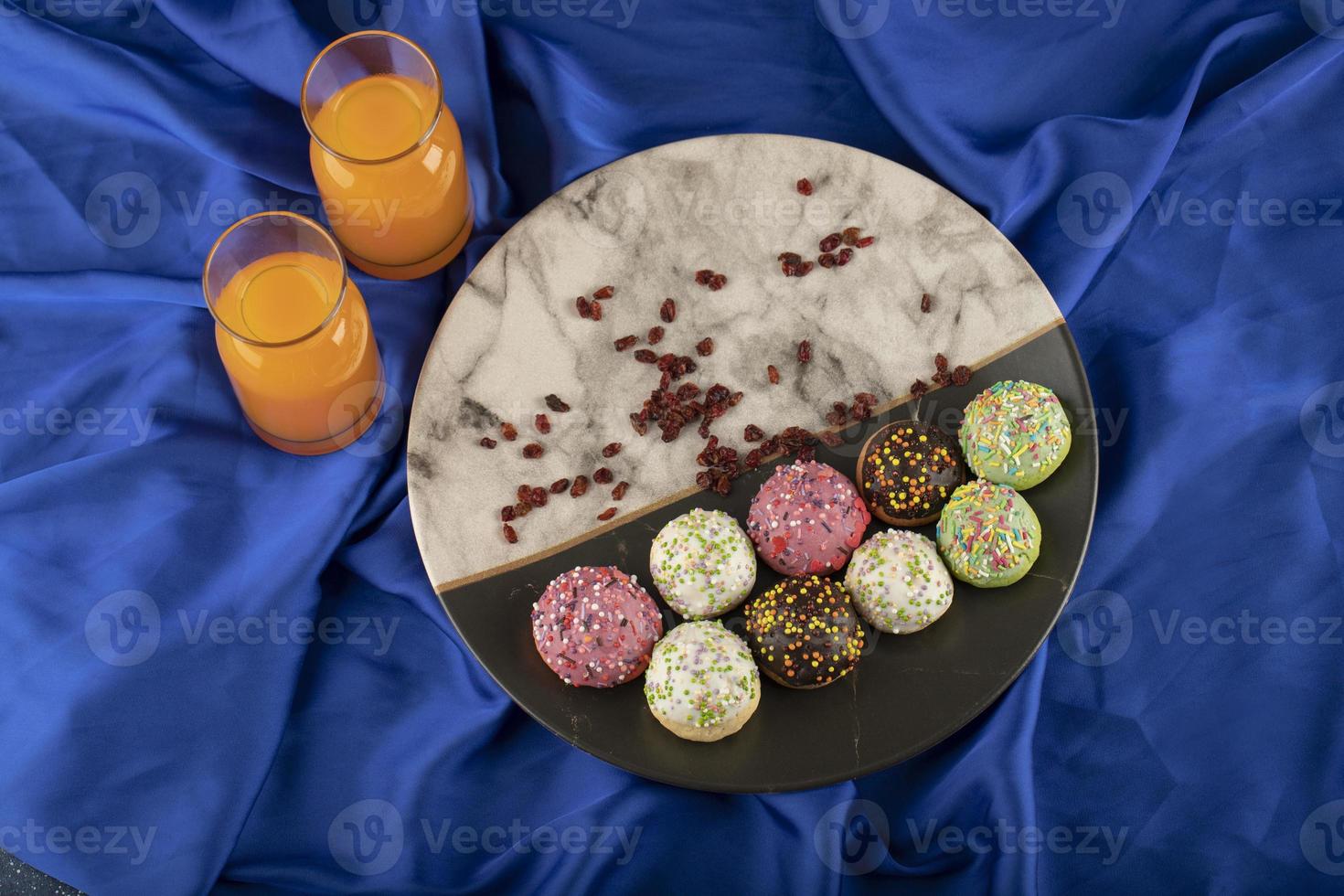 Pequeñas donas dulces de colores con botellas de jugo de naranja foto