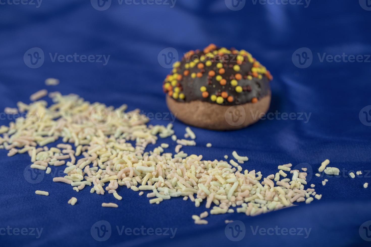 una pequeña rosquilla de chocolate con chispitas sobre un mantel azul foto