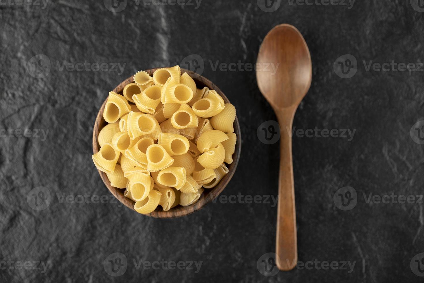 Conchiglie pasta cruda italiana en un recipiente de madera con una cuchara de madera foto