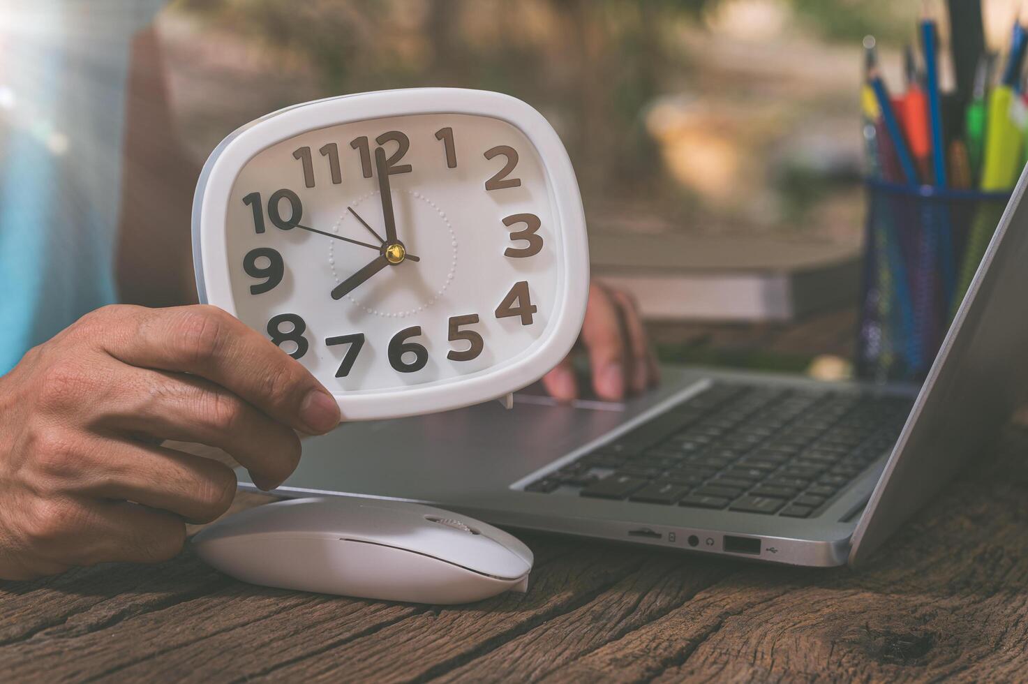 A person's hand holding a clock at a work desk photo