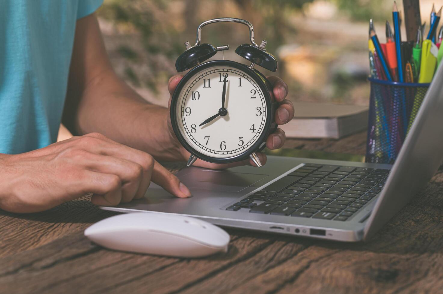 A person's hand holding a clock at a work desk photo