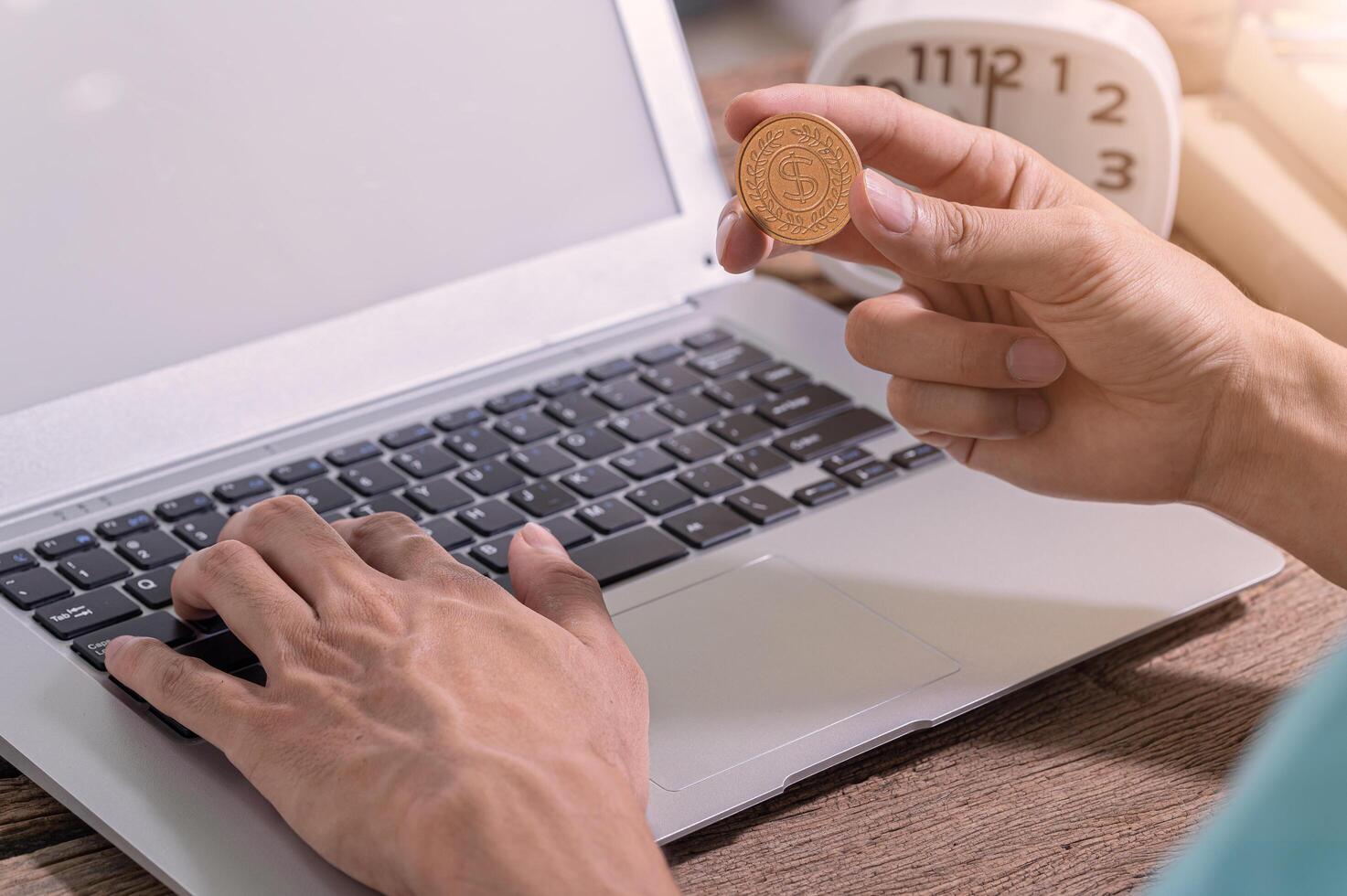 A person using a computer holding a coin, make money online concept photo