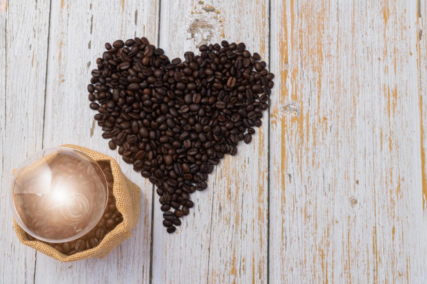 Granos de café en forma de corazón y una bombilla sobre una mesa de madera foto