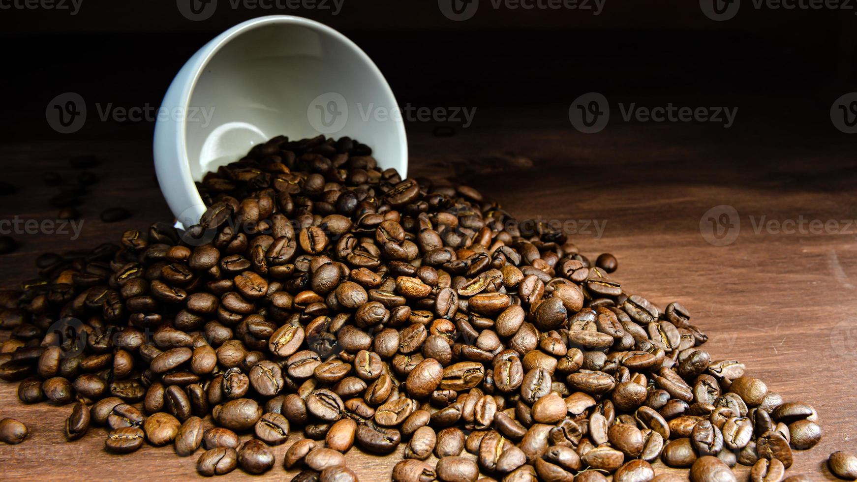 Coffee bean pouring out of a white mug on wooden table photo