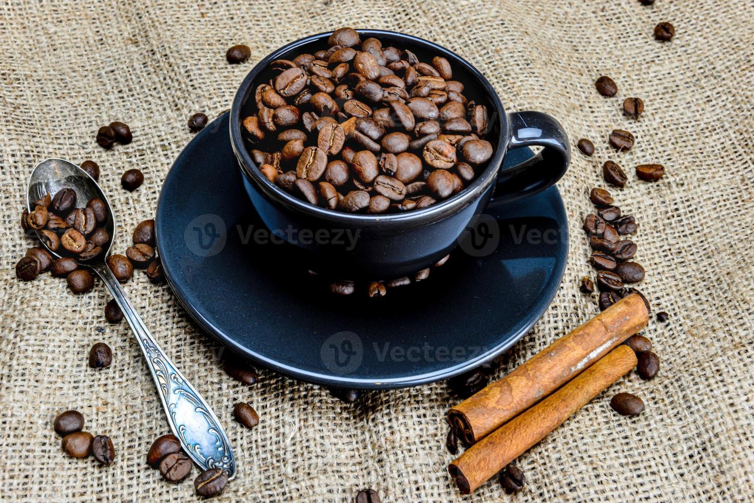 Taza de café negro llena de granos de café orgánico y canela en tela de lino foto