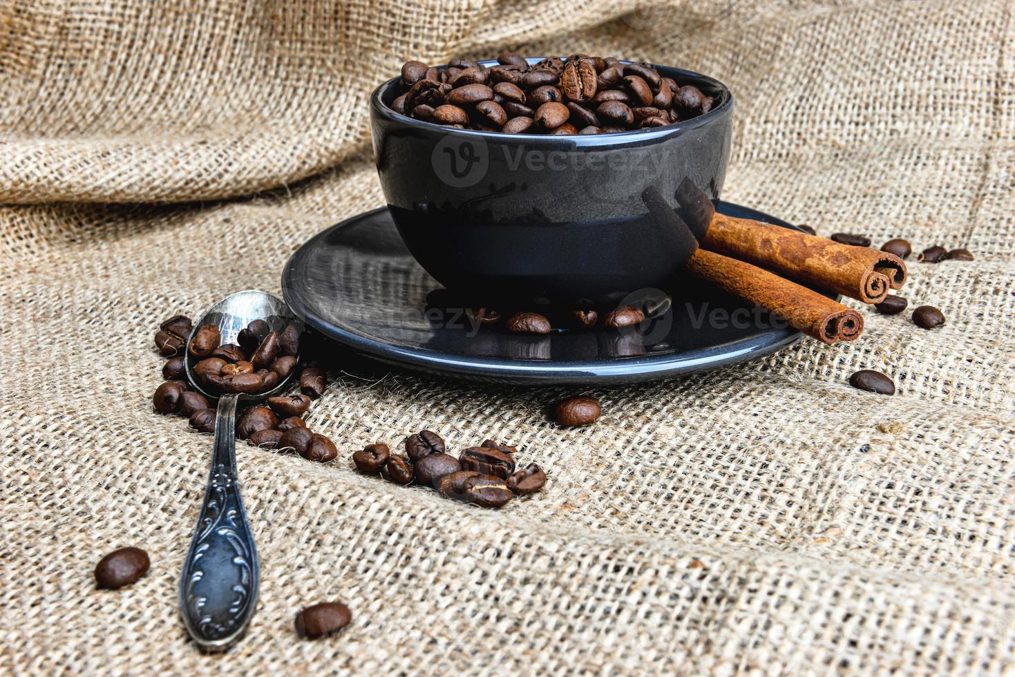 Taza de café negro llena de granos de café orgánico y canela en tela de lino foto