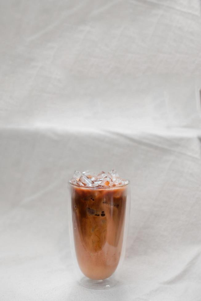 Vaso de café helado con leche sobre fondo de tela blanca foto