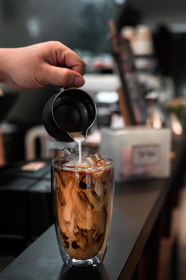 barista vertiendo leche en un vaso de café helado foto