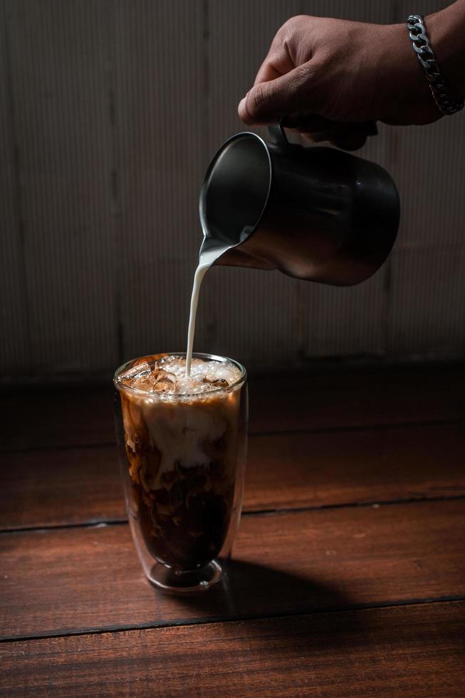 barista vertiendo leche en un vaso de café helado foto