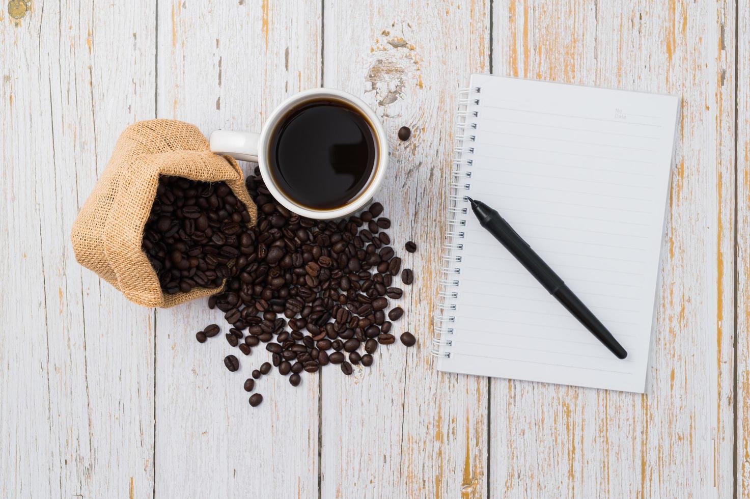 Coffee, coffee beans, and a notebook with a pen on a wooden desk photo