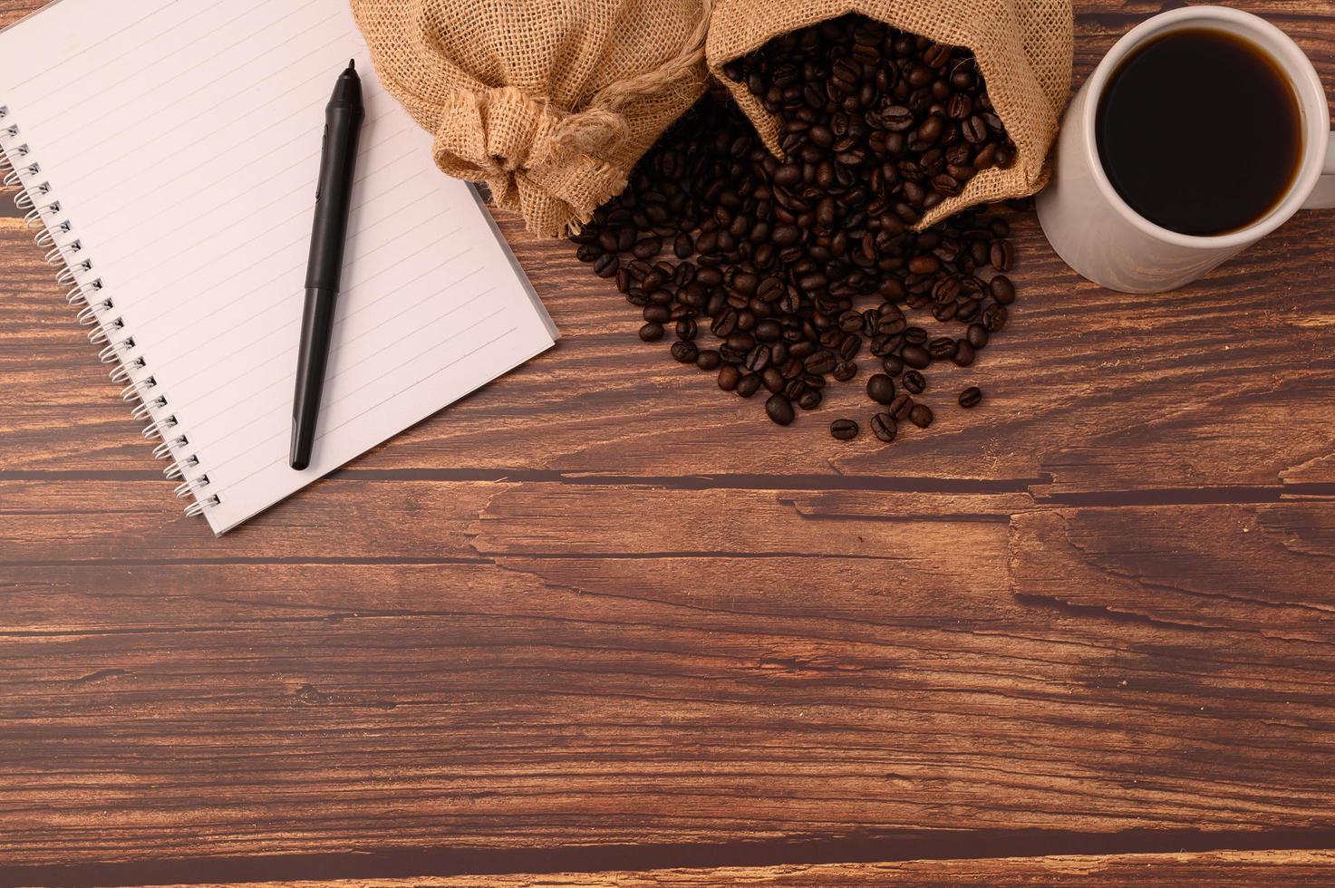café, granos de café y un cuaderno con un bolígrafo en un escritorio de madera foto