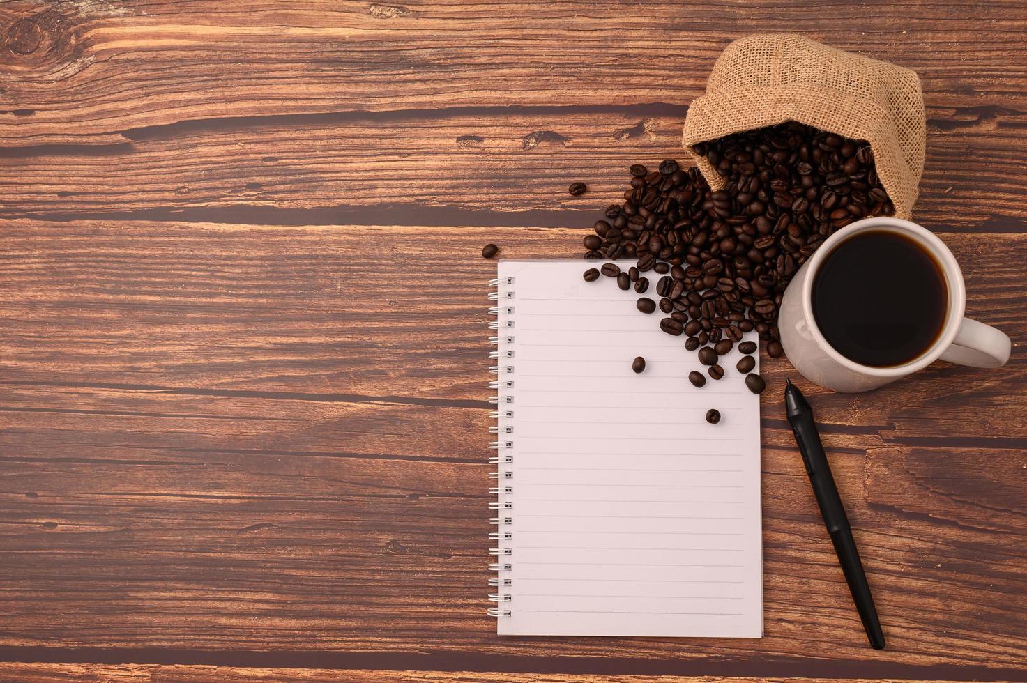 café, granos de café y un cuaderno con un bolígrafo en un escritorio de madera foto