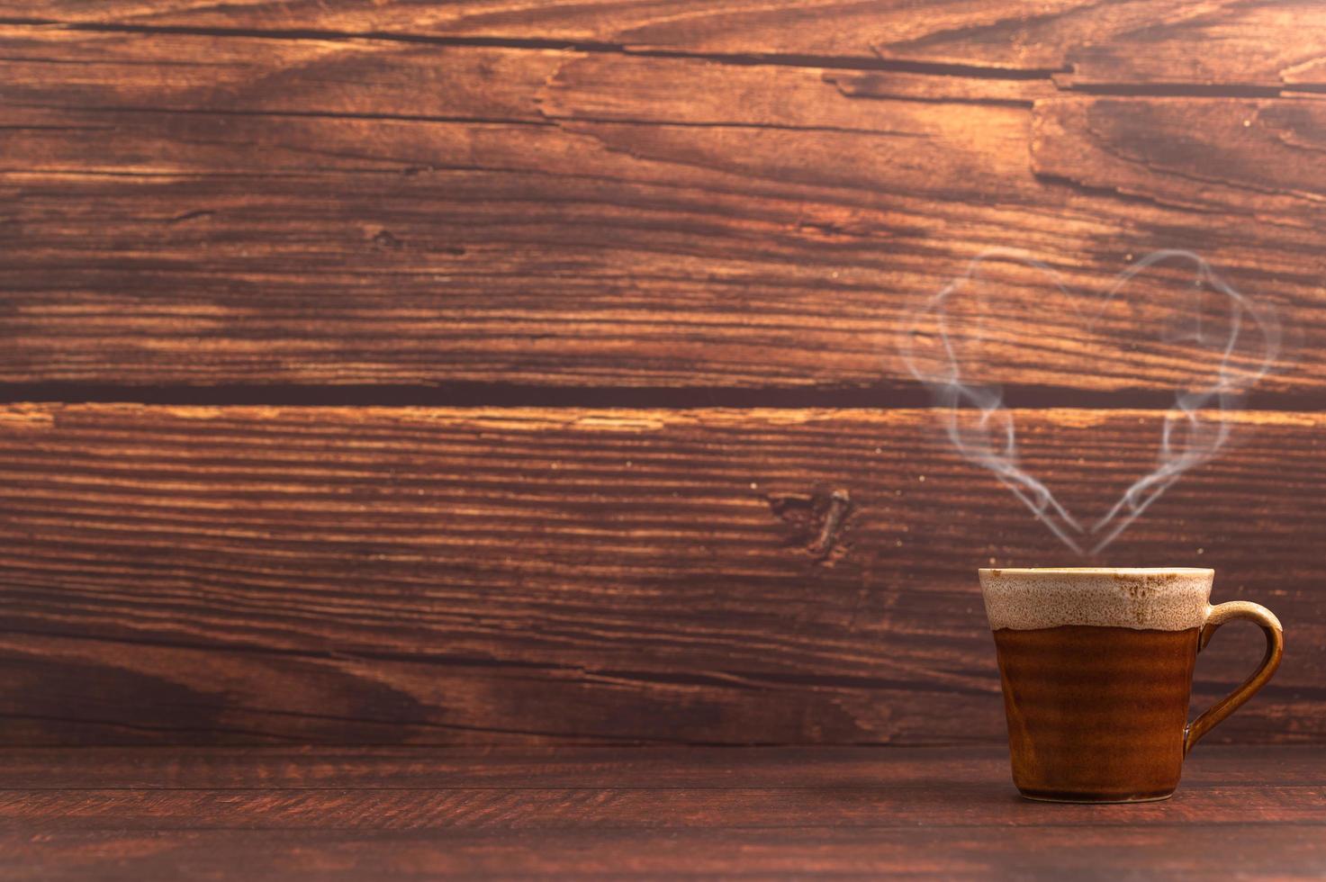 una taza de café haciendo un vapor en forma de corazón sobre una mesa de madera foto