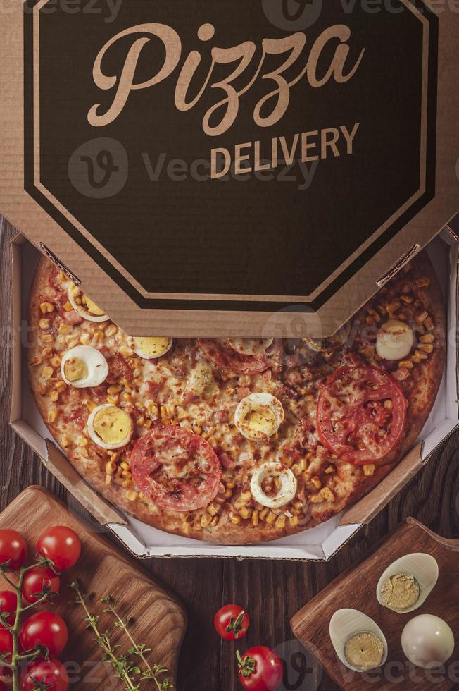 Brazilian pizza with mozzarella, corn, bacon, eggs, tomato and oregano in a delivery box photo