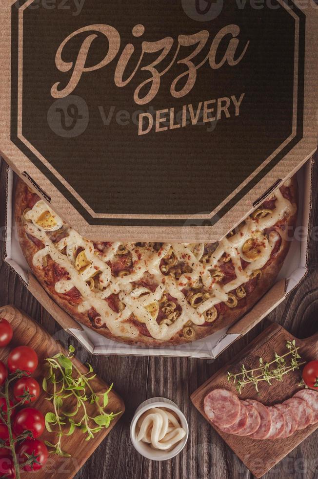 pizza con mozzarella, chorizo calabrese, huevos, catupiry, aceituna y orégano en caja de entrega foto