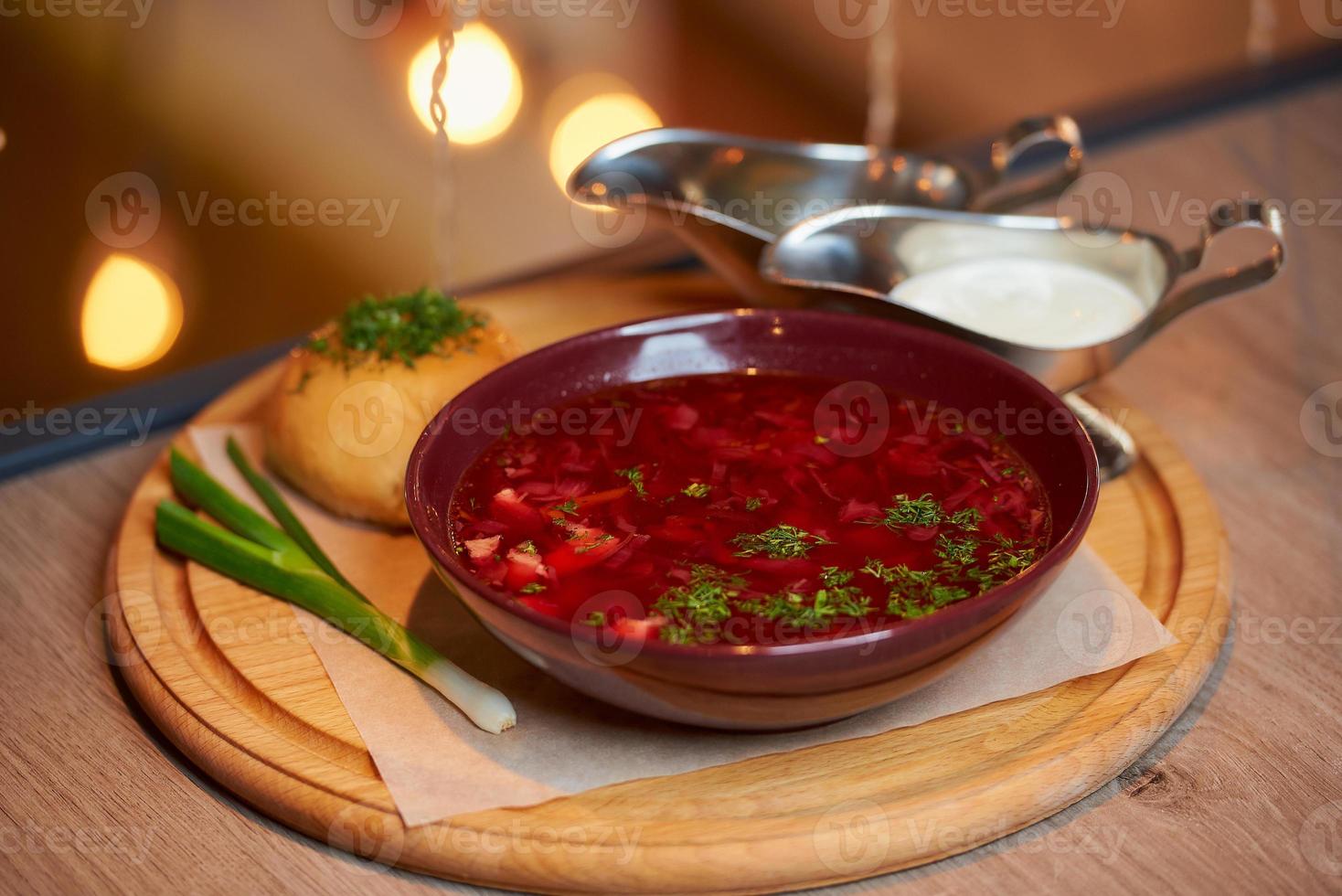 A Ukrainian borsch with a pampushka, onion, and sour cream on a wooden tray photo