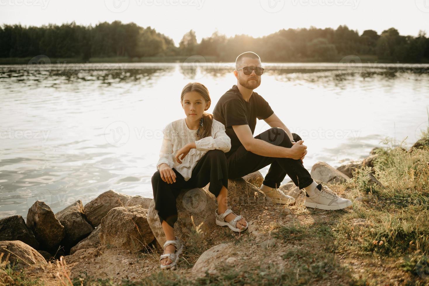 A young father with a beard and sunglasses is posing with his pretty daughter on the coast photo