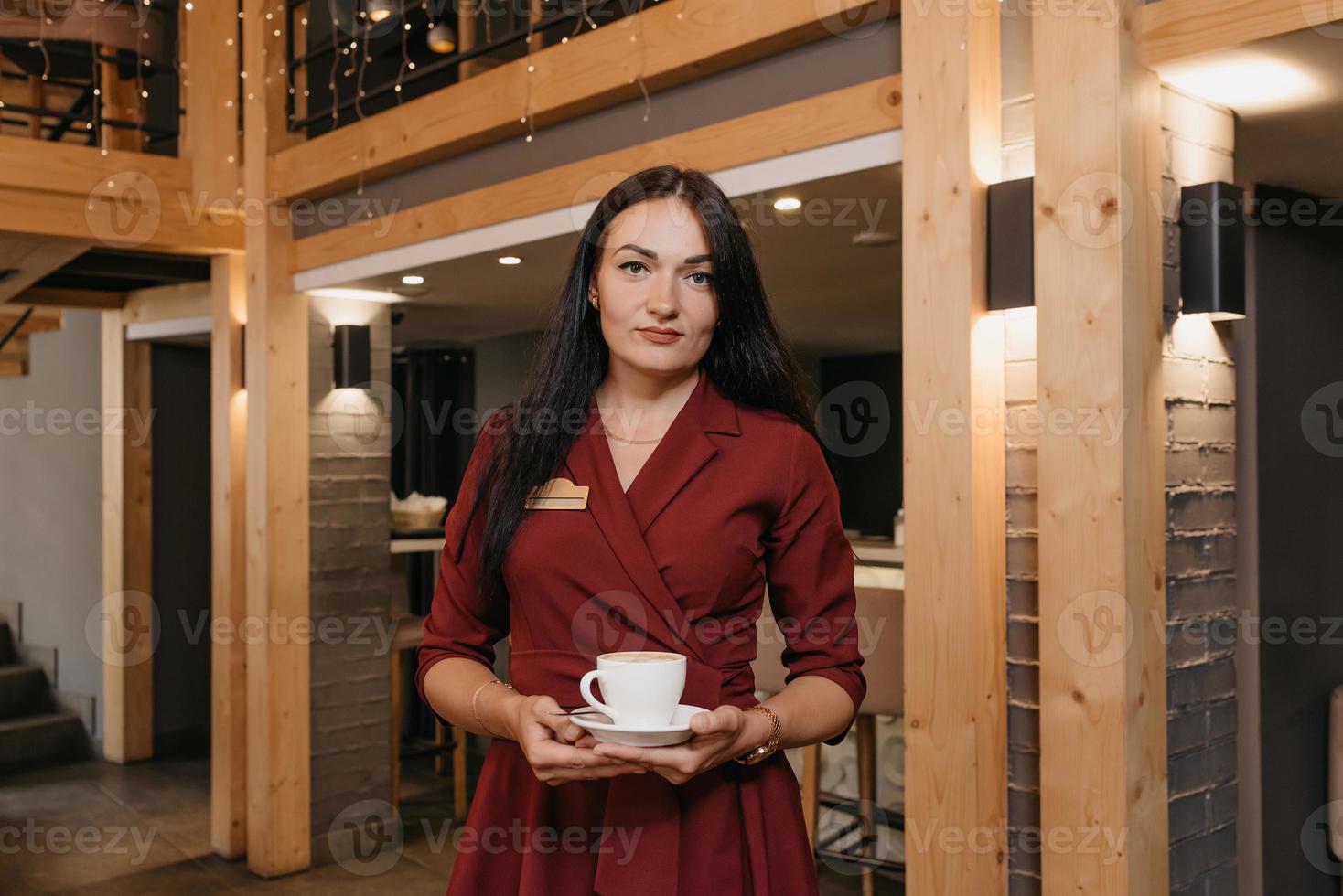 A female restaurant manager wears a black face mask and disposable gloves holding a cup of coffee in a restaurant photo