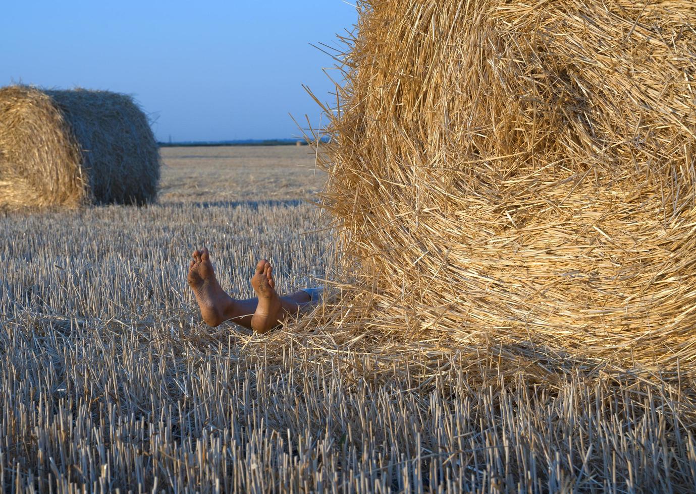 Legs of a person lying down from behind a bale of straw on a farm field photo